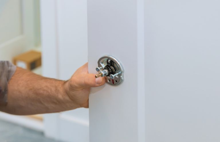 Male carpenter fixing lock in door with home